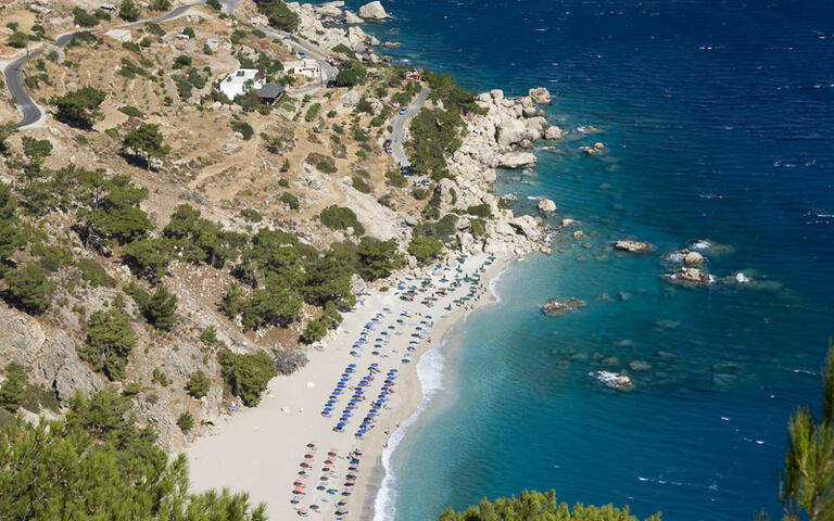 Der weiße Kieselstrand Apella in der Nähe des gleichnamigen Dorfes mit Booten im azurblauen Meer © baldovina / Shutterstock.com